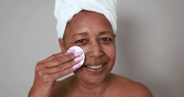 African senior woman taking away skin care face mask with cotton pad - Beauty day concept
