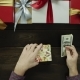 Adult Man Puts Dollars Into Xmas Present Box on Wooden Decorated Table, Top Down Shot - VideoHive Item for Sale