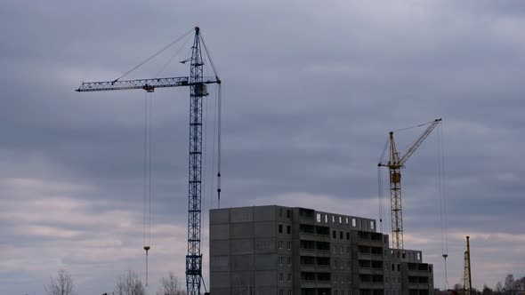 Construction Cranes and a New Building Amid Dark Low Clouds