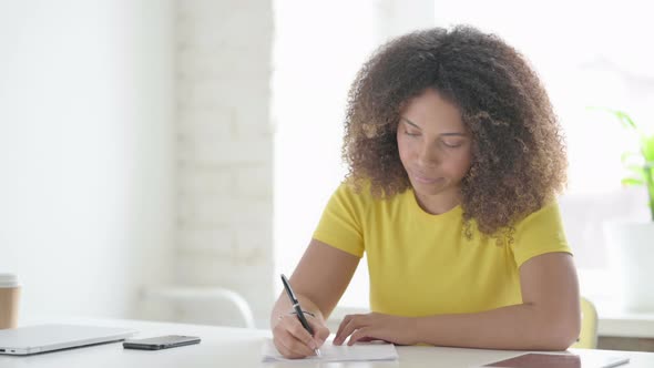 African Woman Writing on Paper in Office