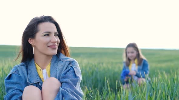 Happy Mother and Daughter Sitting Among Wheat Field on Sky Background