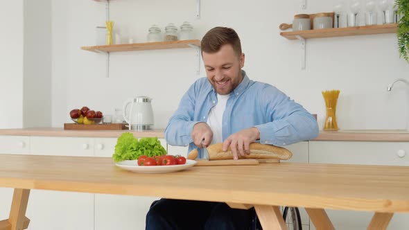 Cheerful Disabled Person in a Wheelchair Cuts Bread in the Kitchen