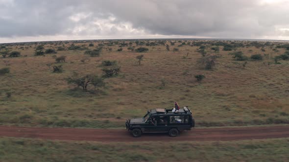 Woman sitting on top of 4 wheel drive while on wildlife safari vacation in Kenya, Aerial drone view