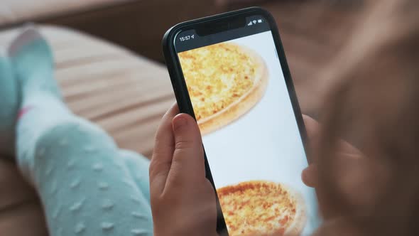 Little girl chooses pizza on smartphone using an application on a mobile phone.