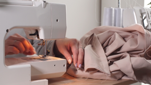 Young Woman Inserts a Light Thread in a Needle of the Sewing Machine