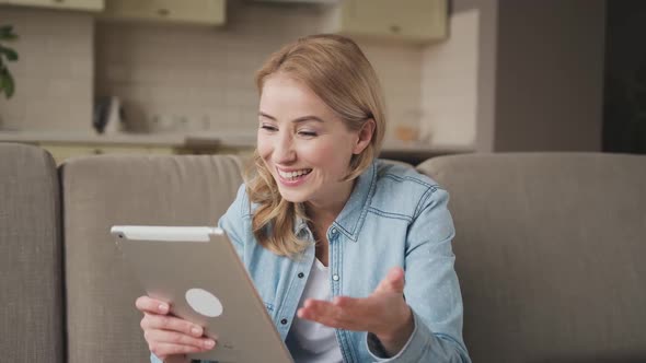 Woman Laughs with a Tablet in Her Hands Sitting on the Couch at Home
