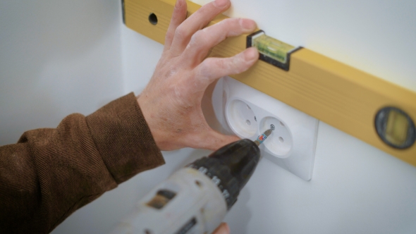 Wireman Is Mounting a Double Socket on a White Wall Inside a Flat, Aligning and Twisting Bolts