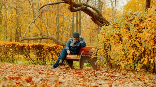 Old Man Is Playing Chess Alone on the Bench in the Autumn Park