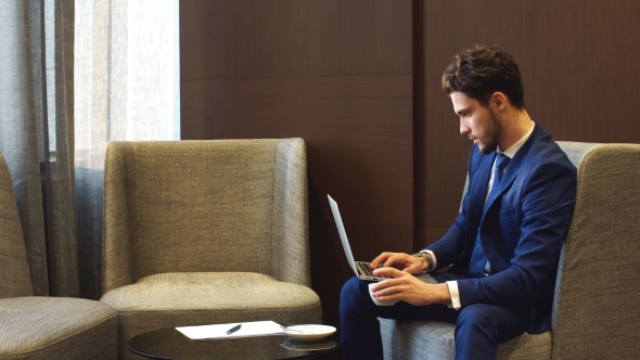 Young businessman in suit working with laptop in cafe