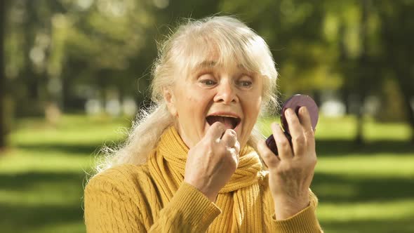 Happy Old Lady Using Lipstick, Sitting on Bench in Park, Anti-Age Cosmetics