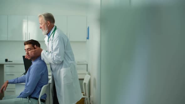 Mature Male Osteopathic Doctor in White Coat Turning and Bending Head of Male Patient to Check His