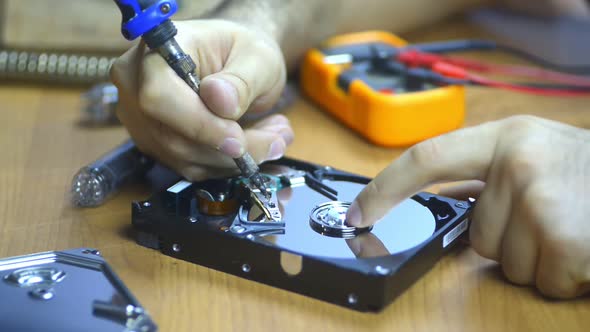 Computer Technician Repairing Hard Drive at Desk with Tools and Electronic Components Technology