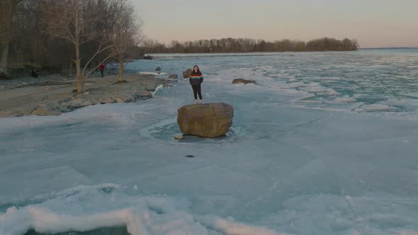 young women wearing pride colors jacket on a Rock in the middle of a frozen lake