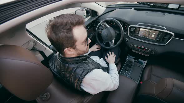 A Man Sits in a Driver Seat While a Car Parks Itself.