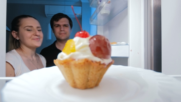 Young Couple Looking for Something To Eat in Fridge and Taking Sweet Cake