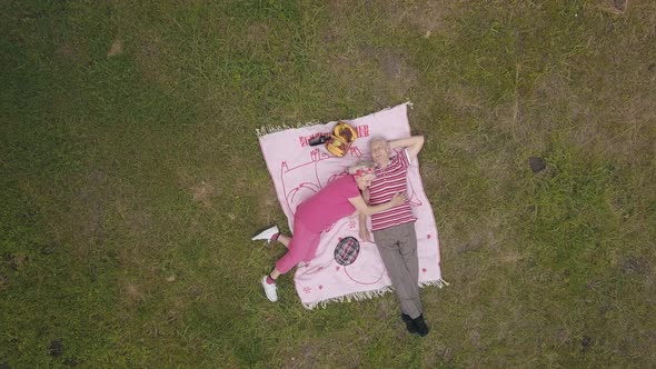Family Weekend Picnic in Park. Aerial View. Senior Old Couple Lie on Blanket on Green Grass Meadow