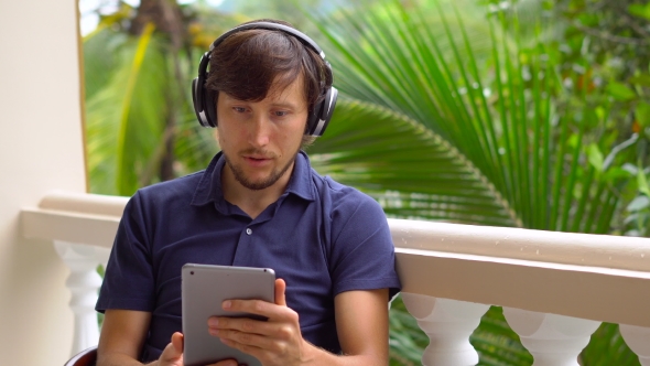Man in Tropics Talking with Friends and Family on Video Call Using a Tablet and Wireless Headphones