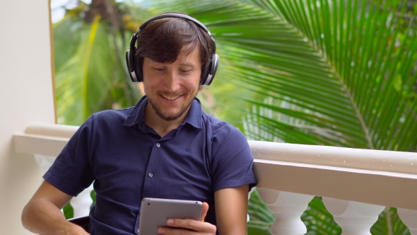 Man in Tropics Talking with Friends and Family on Video Call Using a Tablet and Wireless Headphones