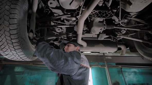 Worker of Car-service Is Checking Backlash in the Suspension of Automobile, He Is Standing Under Car