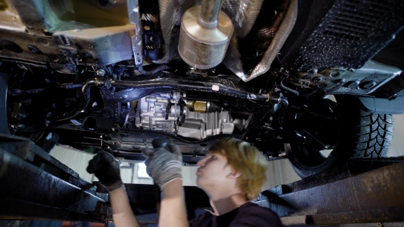 Repairman of Car Workshop Is Standing Under Lifted Automobile and Examining Details