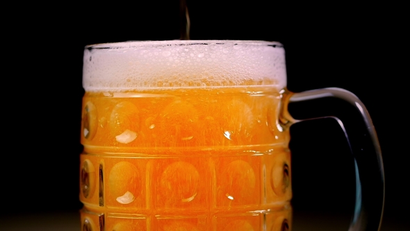 Beer Is Poured Into the Glass on a Black Background. Foam Quickly Slides Through the Glass