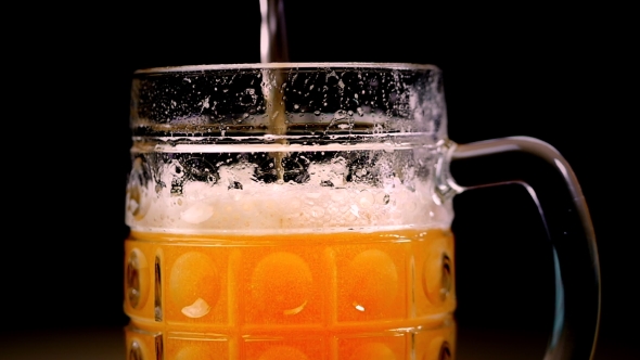 Beer Is Poured Into the Glass on a Black Background. Foam Quickly Slides Through the Glass. Full Mug