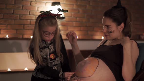 Child Girl Paints Pumpkin on Belly of Pregnant Woman Halloween Night
