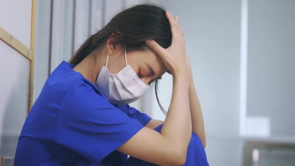 Young Asian Woman Nurse Wearing Uniform and Surgical Mask Looking Distraught on Floor in Hospital