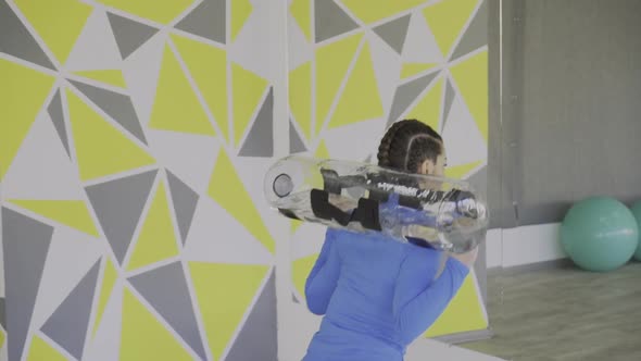 Back View of Female CrossFit Instructor Squatting with Water Bag in Front of Big Mirror