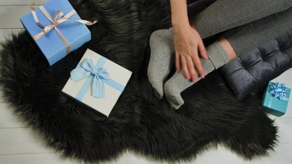 Female Legs in Warm Socks Rest Comfortably on a Gray Fur Skin Next To Blue and White Gift Boxes with