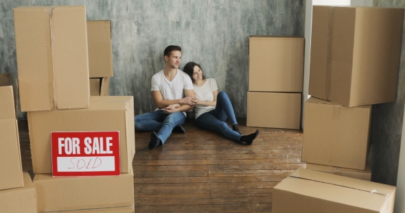 Young Couple Relaxing Laughing After Unpacking Cartons From House Move