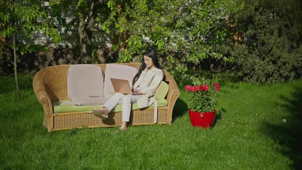 Extreme Wide Shot of Happy Confident Young Asian Woman Sitting in Sunny Garden Texting Typing on