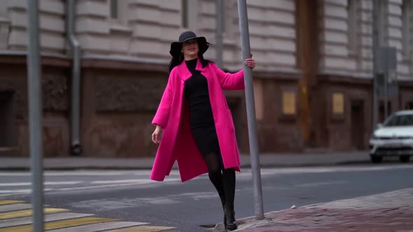 A Fashionable Woman with Black Hair, a Black Hat and a Purple Coat Walks Confidently on the Street