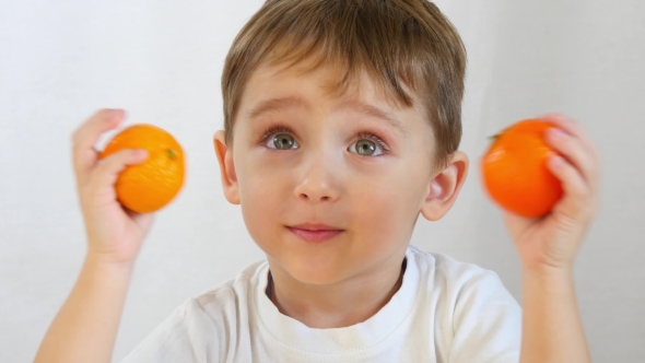 Boy Playing with Tangerines . A Happy Child Sitting at a Table with His Hands, Puts Them To His