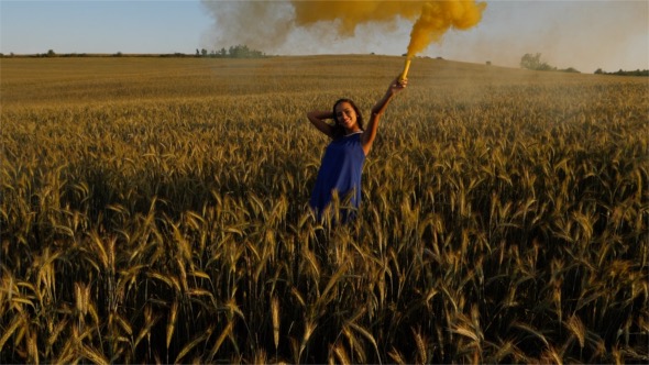 Beautiful Girl with Coloured Smoke in a Wheat Field