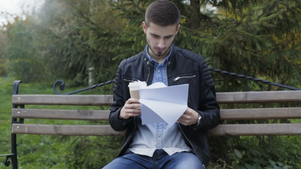 Handsome Man Drinks Coffee and Works with Papers in Park
