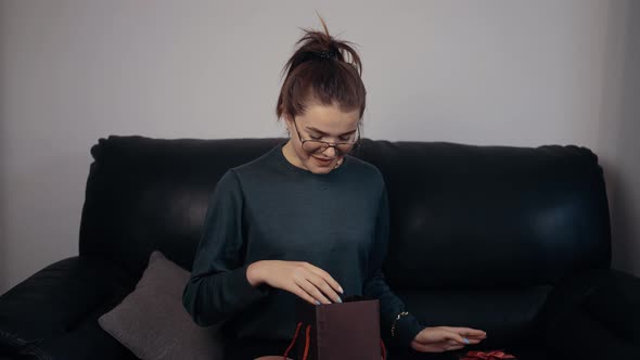 The Young Redhead with Glasses That Opens the Gift and Surprised Looks at Its Contents