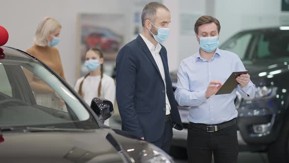 Young Dealer Consulting Client in Car Dealership on Coronavirus Pandemic