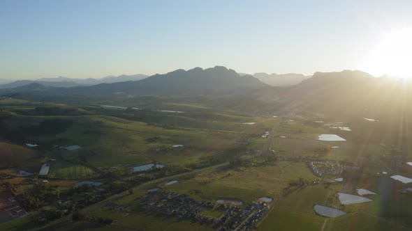 Sun rays sunrise over homes in vineyards farmland with ponds, Stellenbosch, Aerial Drone
