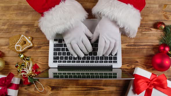 Top View Santa Hands in White Gloves Typing on Keyboard By Wooden New Year Decorated Table