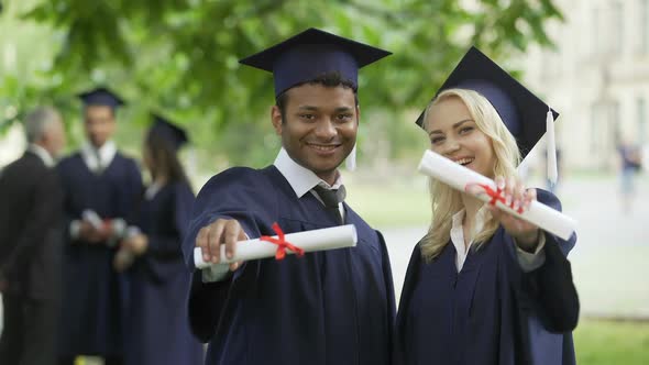 Male and female graduates showing diplomas and smiling, complete high education