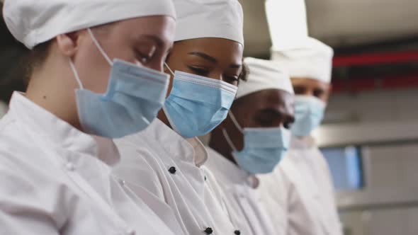 Diverse group of chefs wearing face masks standing in restaurant kitchen