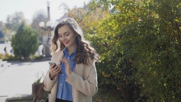 Beautiful Girl in a White Coat Uses a Smartphone and Smiling