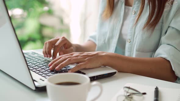 Young woman with cup of coffee sitting at living room and working on laptop at home