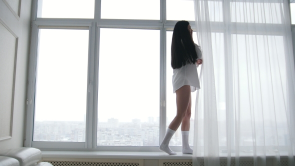 Beautiful Young Woman in a White Men's Shirt and Socks Walking on Windowsill and Talking on the