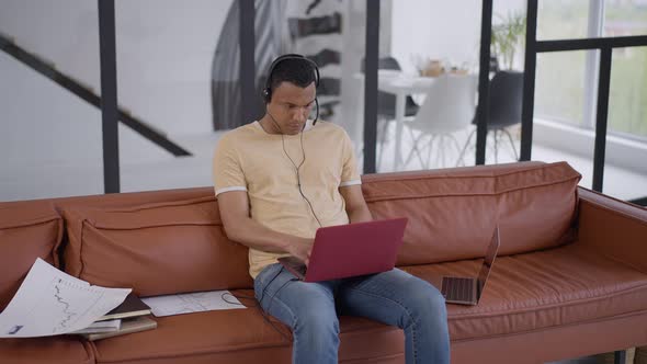 Busy Man in Headphones Typing on Laptop Keyboard Sitting in Home Office Living Room on Couch