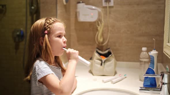 Girl Brushes Teeth in Bathroom with an Electric Toothbrush
