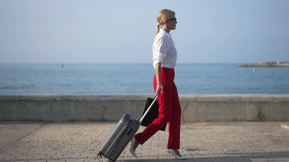 Side View of Gorgeous Slim Confident Businesswoman with Travel Bag Walking in Slow Motion Along Blue