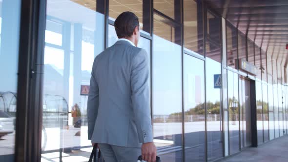 Elegant businessman walking with suitcase along the airport. Young mail entrepreneur.