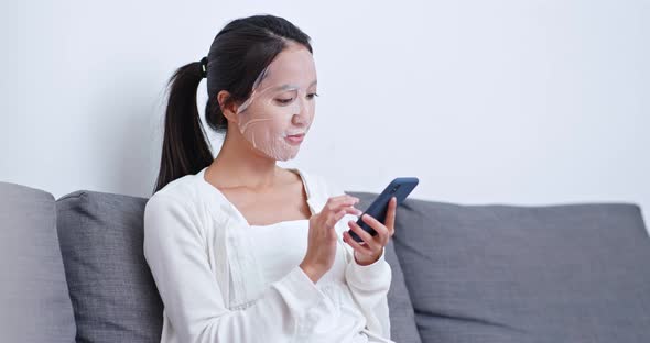 Woman apply paper mask on face and use of cellphone at home